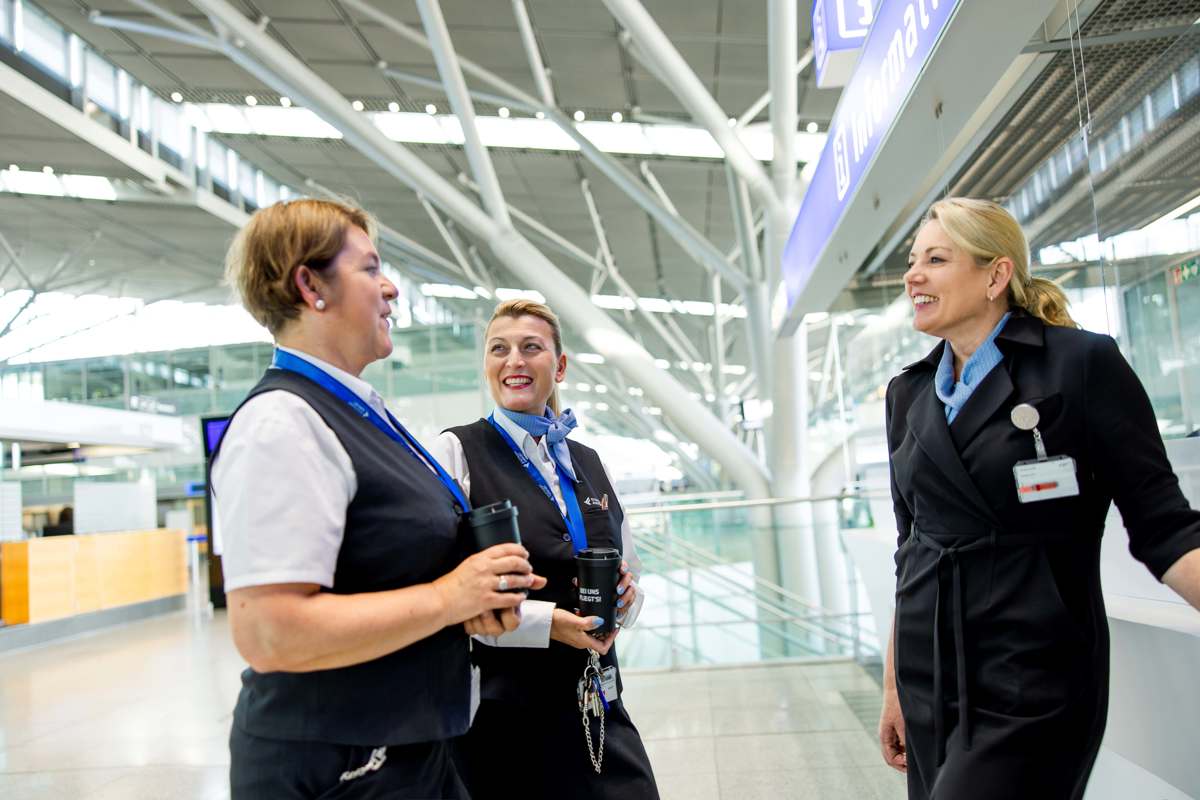 Drei Mitarbeiterinnen des Flughafen Stuttgart stehen am Informationsschalter und sprechen miteinander.
